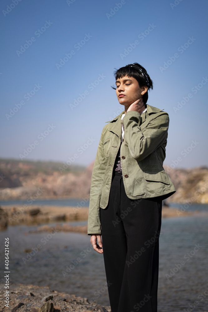 A young beautiful indian girl standing neat a lake in the mountains with a hand on her neck, wearing a denim jacket and black pants. A young beautiful indian girl standing neat a lake in the mountains with a hand on her neck, wearing a denim jacket and black pants.