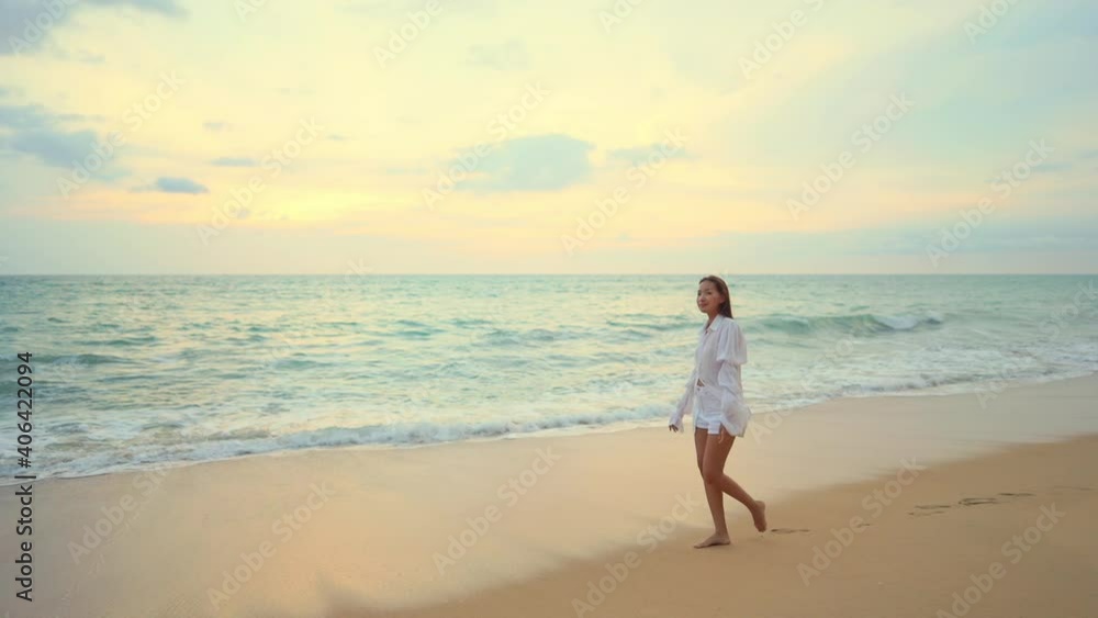 Young girl slowly walking barefoot along the shore near the ocean with waves reaching the wet sand during sunset. Young girl slowly walking barefoot along the shore near the ocean with waves reaching the wet sand during sunset.