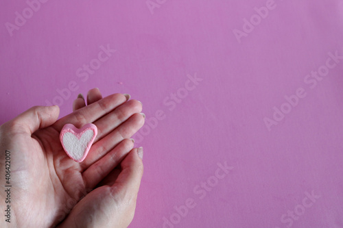 Isolated marshmallow heart shape on woman s hand with pink background for Valentine s day