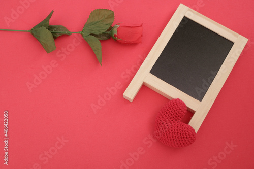 Top view of blackboard with red flower and crochet handmade red heart on red background for Valentine's day