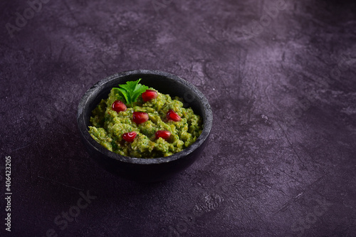 Stone black bowl with spinach and pomegranate seeds appetizer on a dark gray background.
