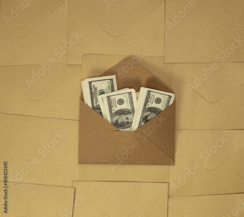 Craft paper envelope with one hundred dollar bills on brown plain background top view, copy space, business and financial concept background photo
