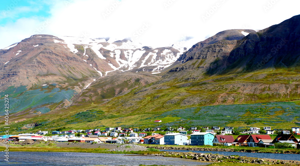 The beautiful town overlooking the partially snowy mountain the summer near Olafsjordur, Iceland