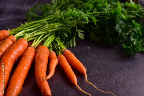 Fresh carrots with green stems and leaves on a dark gray granite background.
