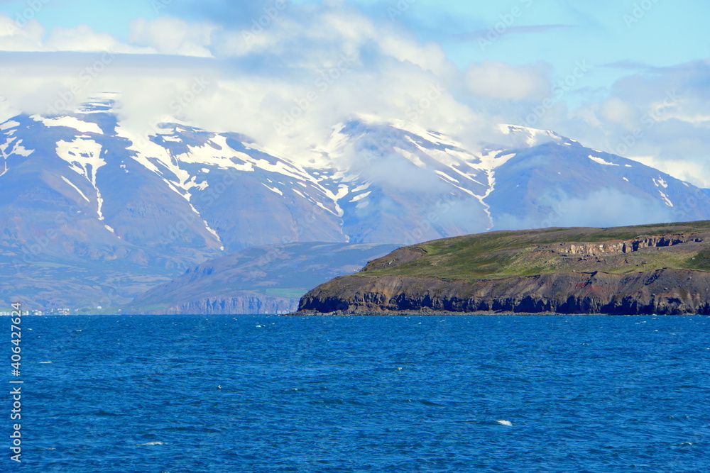 Beautiful blue fjord and the hills overlooking partially covered snowy mountain in the summer near Hofn, Iceland