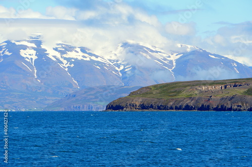 Beautiful blue fjord and the hills overlooking partially covered snowy mountain in the summer near Hofn, Iceland