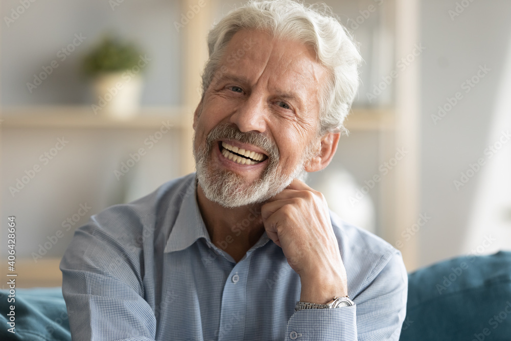 Head shot portrait of happy middle aged older retired man laughing at funny joke. Emotional smiling elderly grandfather looking at camera, enjoying video call or distant communicating with friends. Head shot portrait of happy middle aged older retired man laughing at funny joke. Emotional smiling elderly grandfather looking at camera, enjoying video call or distant communicating with friends.