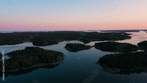 Aerial view of a boat driving in middle of the archipelago, purple dusk sky, in Scandinavia - rising, tilt, drone shot photo