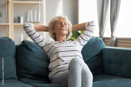 Billede på lærred Happy middle aged elderly hoary woman relaxing on comfortable couch with folded hands behind head, sleeping or napping alone indoors