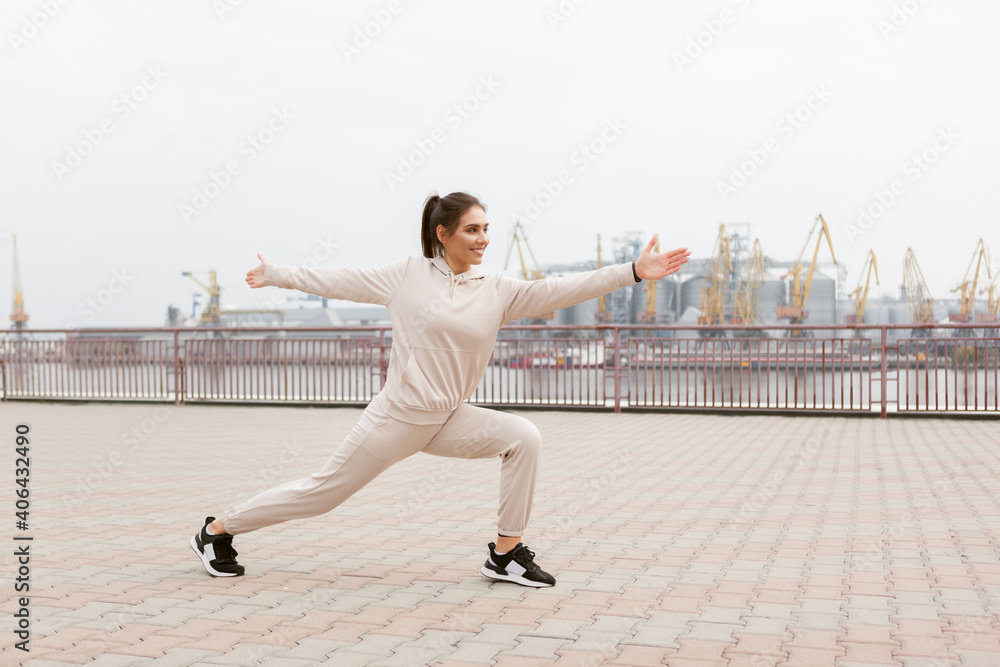 Fototapeta premium Healthy fit woman practicing yoga asana exercises on the background of an industrial city. Warrior 2 pose