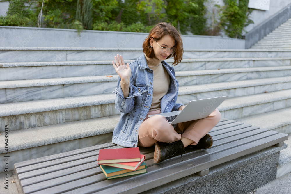 Young pretty student woman sitting with laptop. Caucasian girl have online call outdoors. Young pretty student woman sitting with laptop. Caucasian girl have online call outdoors.
