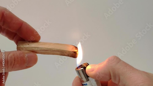 A Palo Santo stick is light up with a lighter. The flame starts to grow on the sitck and is then turned off by shaking the stick. The smoke which is used as air freshner starts to spread around. photo