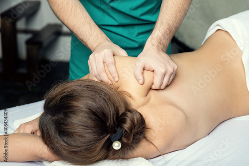 Massage therapist doing massotherapy of a young woman. Beautiful relaxed face of a young woman with brown hair and closed eyes