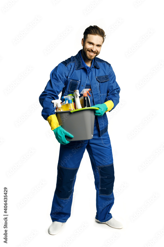 Attractive young man in cleaning uniform holding a bucket of cleaning products in his hands, isolated on white background Attractive young man in cleaning uniform holding a bucket of cleaning products in his hands, isolated on white background