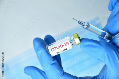 A doctor wearing blue gloves holds a bottle of COVID-19 vaccine.