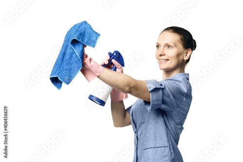 A beautiful young woman in the uniform of a maid holds a rag and spray for washing windows and looks at them with smile. Isolated on a white background