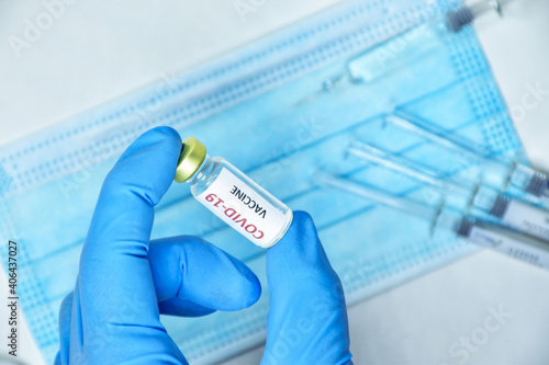 A doctor wearing blue gloves holds a bottle of COVID-19 vaccine.