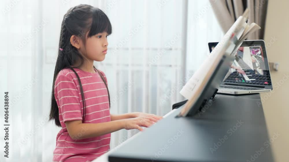 Asian young girl learning piano lesson online at home by e-learning.