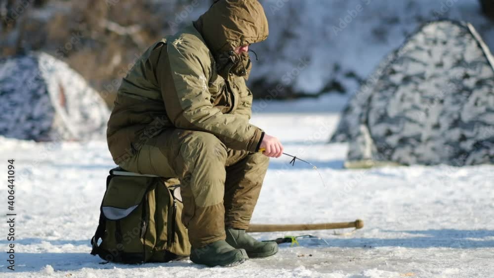 A fisherman sits on a box and catches fish in winter in sunny weather A fisherman sits on a box and catches fish in winter in sunny weather