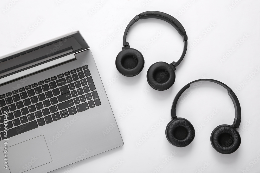 Laptop and two pairs of black wireless stereo headphones on white background Laptop and two pairs of black wireless stereo headphones on white background