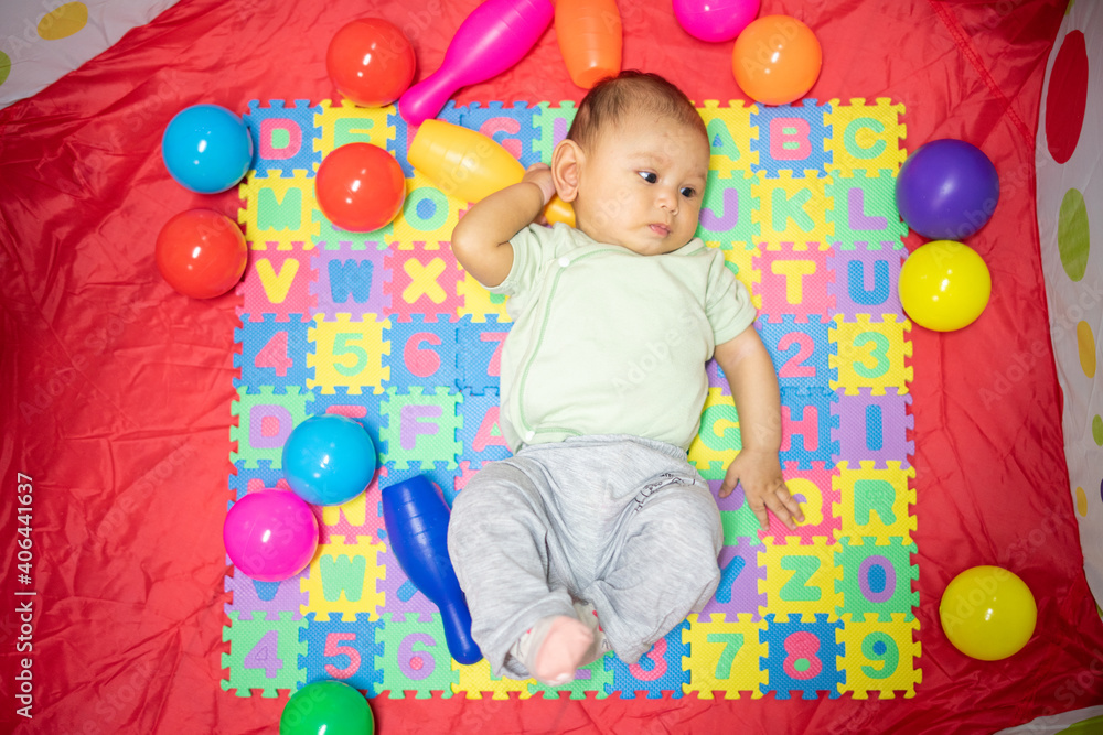 Obraz premium 3-4 Month Old Baby GIrl lying on play mat playing with colored toys developing her eyes and motor skills, young baby girl grasping and holding her toys
