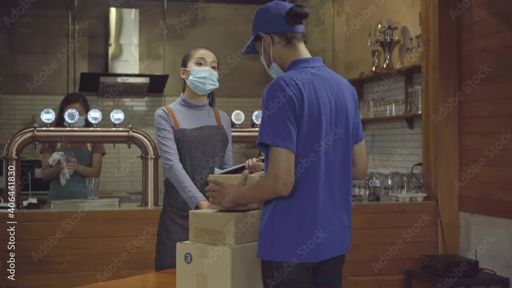 The restaurant manager wears a face mask receiving product boxes from supplier sent via delivery service The restaurant manager wears a face mask receiving product boxes from supplier sent via delivery service