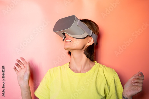 Emotional portrait of woman in virtual reality glasses in studio on pink orange background