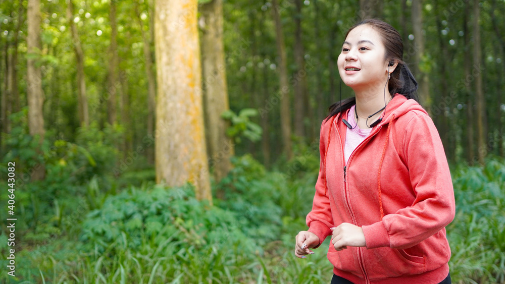 Asian woman running in forest wearing jacket and earphone Asian woman running in forest wearing jacket and earphone