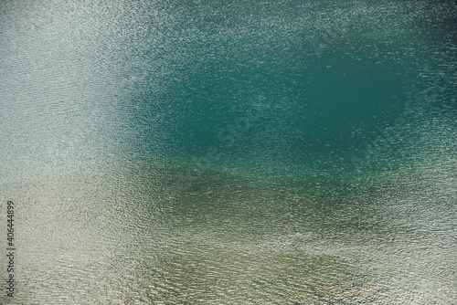 Texture of green blue calm water of lake. Meditative ripples on water surface. Nature minimal background of green blue lake with golden shine. Natural backdrop of lake fragment with clear azure water.