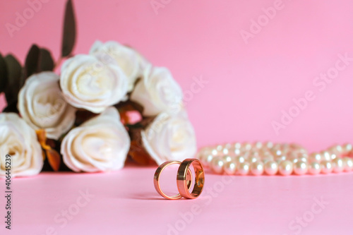 Wedding ring with blurry white rose and pearl necklace on the background isolated on pink