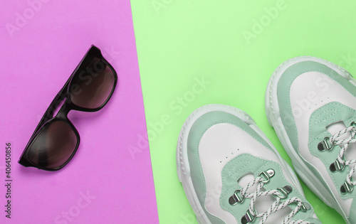 Fashionable sneakers with sunglasses on green purple pastel background. Top view. Minimalism
