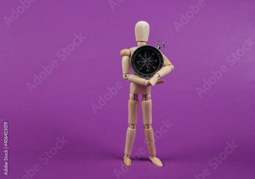 Wooden puppet holds a compass on a purple background. Business or travel concept photo