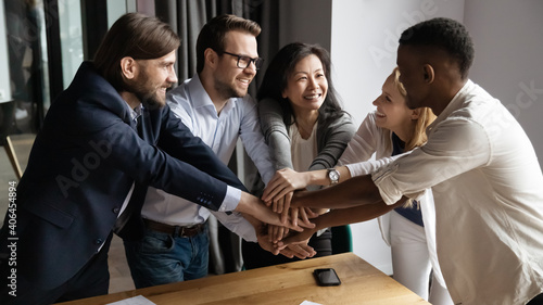 Canvas Print Excited happy young and mature mixed race colleagues joining hands, strengthening team spirit, motivating each other at meeting