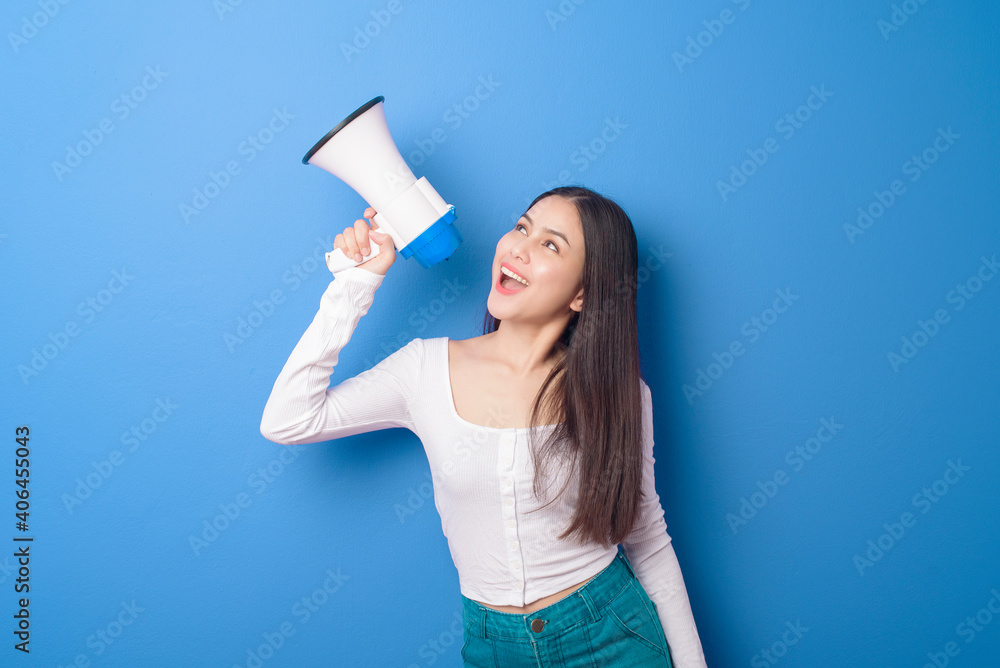 portrait of young beautiful smiling woman is using megaphone to announce over isolated blue background studio portrait of young beautiful smiling woman is using megaphone to announce over isolated blue background studio