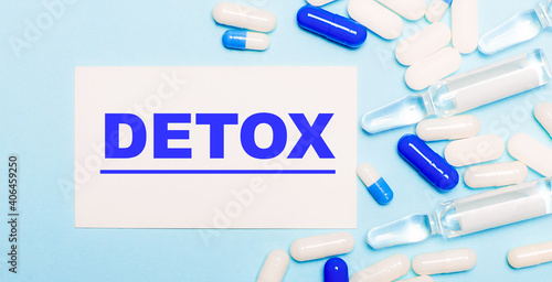 Pills, ampoules and a white card with the text DETOX on a light blue background. Medical concept