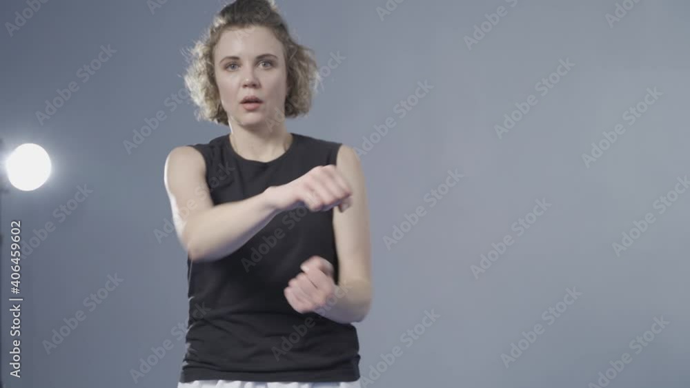 Female fighter throws punches directly into camera. Woman athlete tekwando strikes sharp, quick strikes, looking directly into camera, quick movements against wall. Self defense concept for women Female fighter throws punches directly into camera. Woman athlete tekwando strikes sharp, quick strikes, looking directly into camera, quick movements against wall. Self defense concept for women