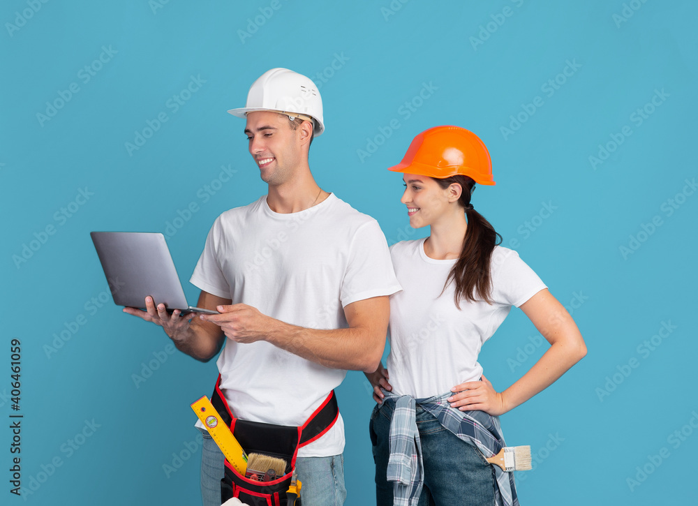 Happy young couple in hardhats using laptop, ordering materials for repair apartment Happy young couple in hardhats using laptop, ordering materials for repair apartment