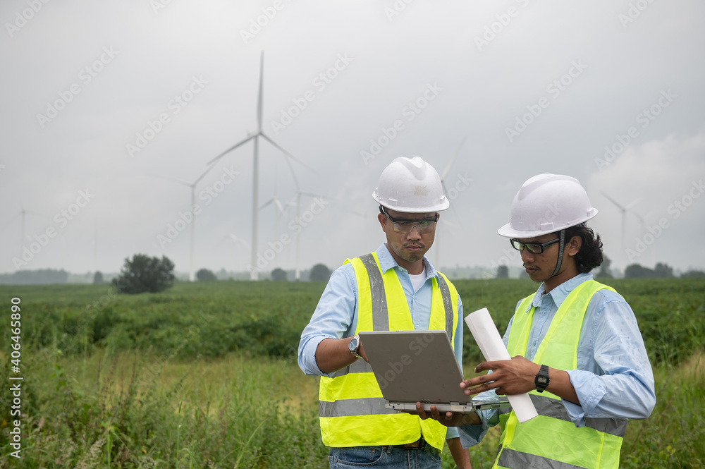 Two engineers working and holding the report at wind turbine farm Power Generator Station on mountain,Thailand people Two engineers working and holding the report at wind turbine farm Power Generator Station on mountain,Thailand people