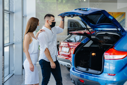 Young couple in masks selects a new vehicle and consult with a representative of the dealership in the period of the pandemic. Car sales, and life during the pandemic