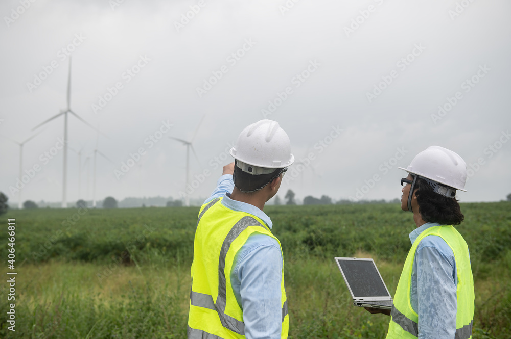 Two engineers working and holding the report at wind turbine farm Power Generator Station on mountain,Thailand people Two engineers working and holding the report at wind turbine farm Power Generator Station on mountain,Thailand people
