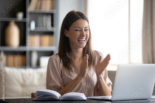 Overjoyed young woman looking at laptop screen, surprised by good news, looking at laptop screen, sitting at work desk at home, excited female celebrating success, clapping hands, online win