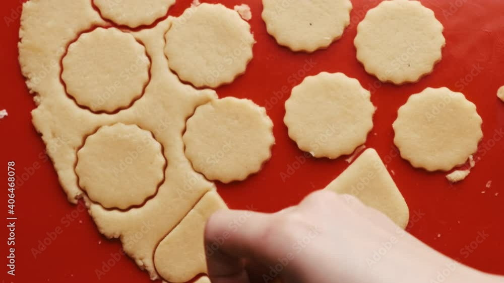 Woman hands takes cookies in the shape of heart and round for St. Valentines Day using red plastic mold on the red silicone baking mat. Woman hands takes cookies in the shape of heart and round for St. Valentines Day using red plastic mold on the red silicone baking mat.