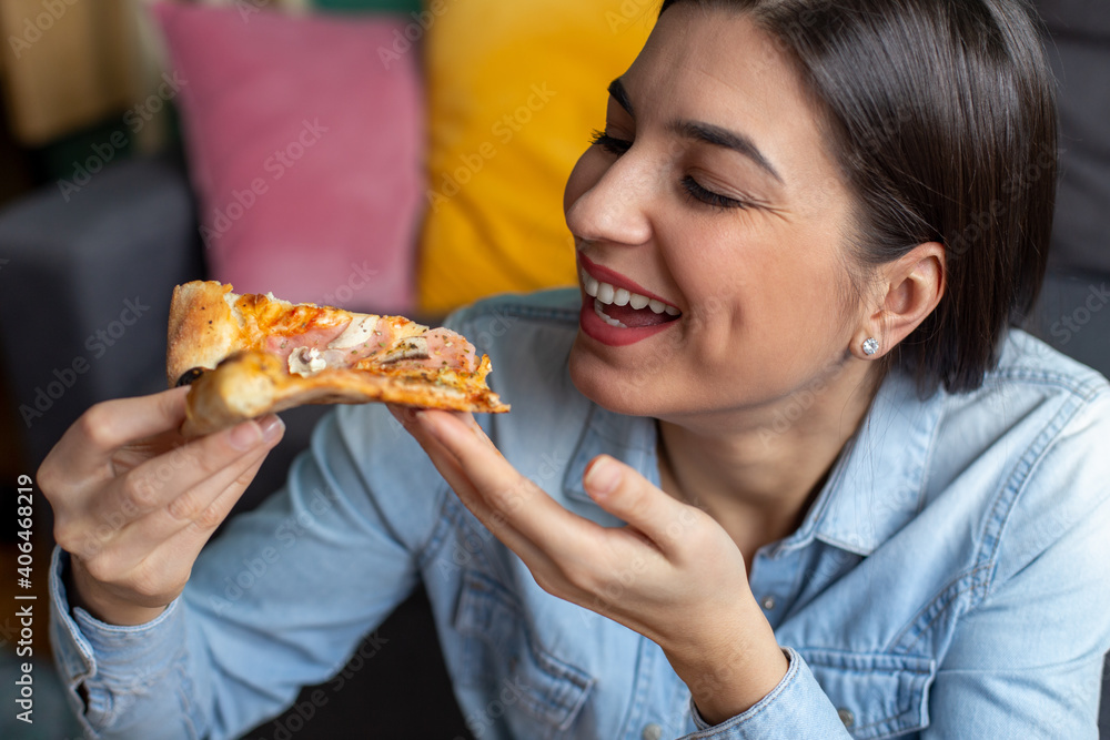 A young brunette woman is eating pizza at home.