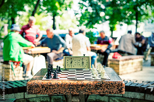 Chess board with pieces and clock on wooden desk In connection with the chess tournament. Chess pieces and stopwatch on a board in the park. toned