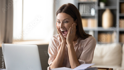 Close up overjoyed surprised woman looking at laptop screen, sitting at work desk, reading good unexpected news in email, message, excited by money refund, job promotion or great sale offer