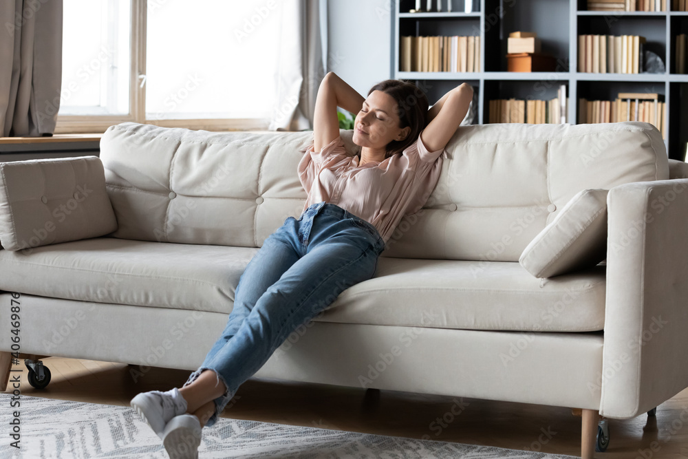 Obraz premium Full length calm woman with closed eyes resting on cozy couch, leaning back, enjoying lazy leisure time, attractive peaceful young female relaxing, daydreaming, taking nap on sofa at home
