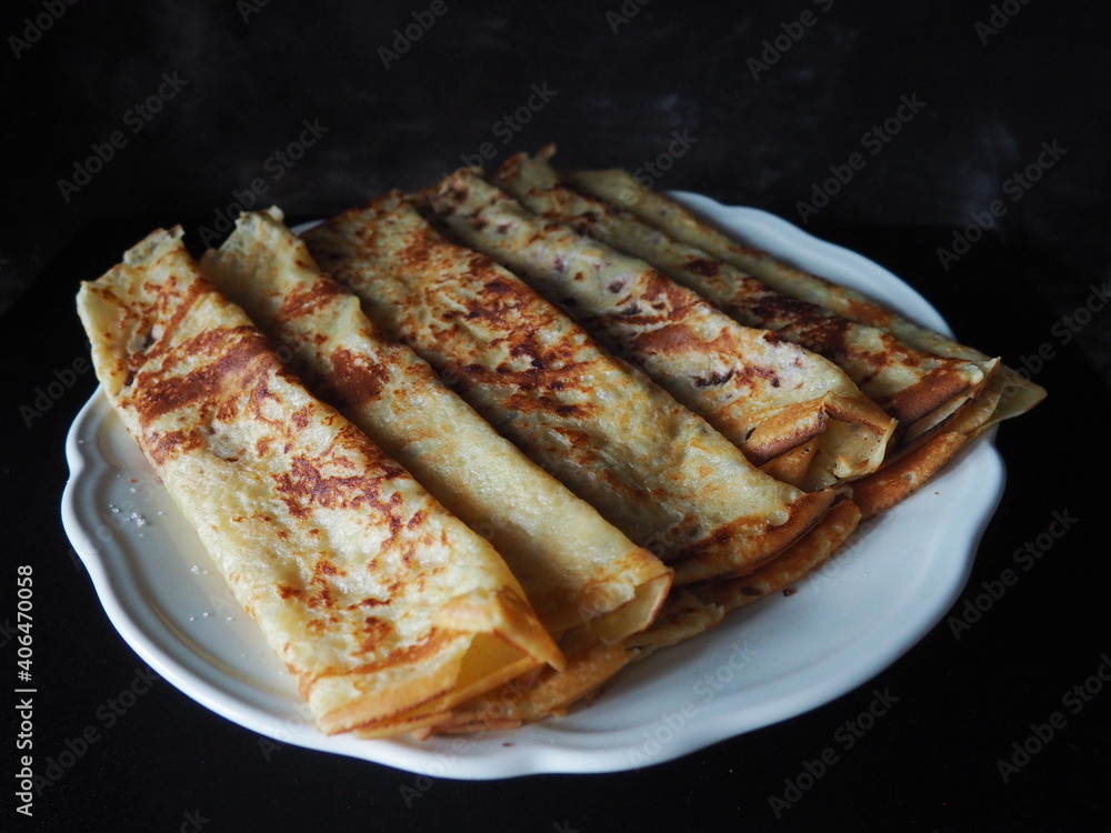 Homemade crepes, french crêpes, traditionally made for Candlemas, on black background, showing the whole plate, horizontal picture