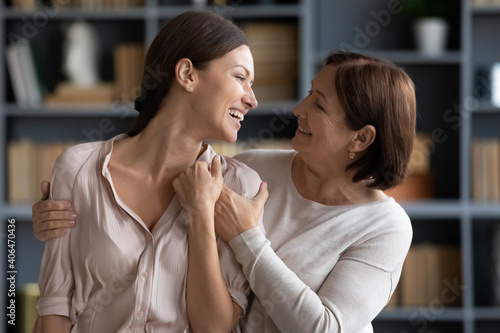 Close up overjoyed young woman and mature mother having fun, laughing, enjoying pleasant conversation, elderly mum and grownup daughter hugging, standing at home, good family relationship