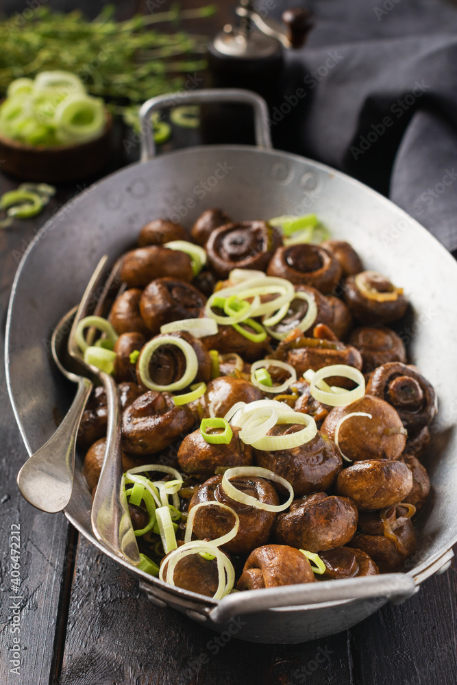 Mushrooms champignon fried in soy sauce, with pepper and steamed onions in an old metal bowl on an old vintage table. Selective focus. Mushrooms champignon fried in soy sauce, with pepper and steamed onions in an old metal bowl on an old vintage table. Selective focus.