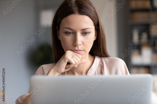 Close up thoughtful woman touching chin, pondering strategy, looking at laptop screen, reading news in email, serious focused female student searching information, working on online project photo